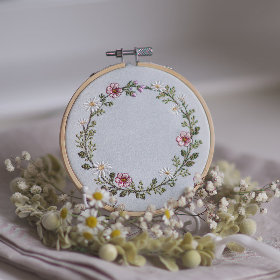 Stickdatei Wiesenkranz 10x10 mit Margeriten, rosa Wildblumen und Kräutern als runder floraler Rahmen auf Leinen, ideal für Kissen, Patchwork und personalisierte Stickprojekte im Landhausstil