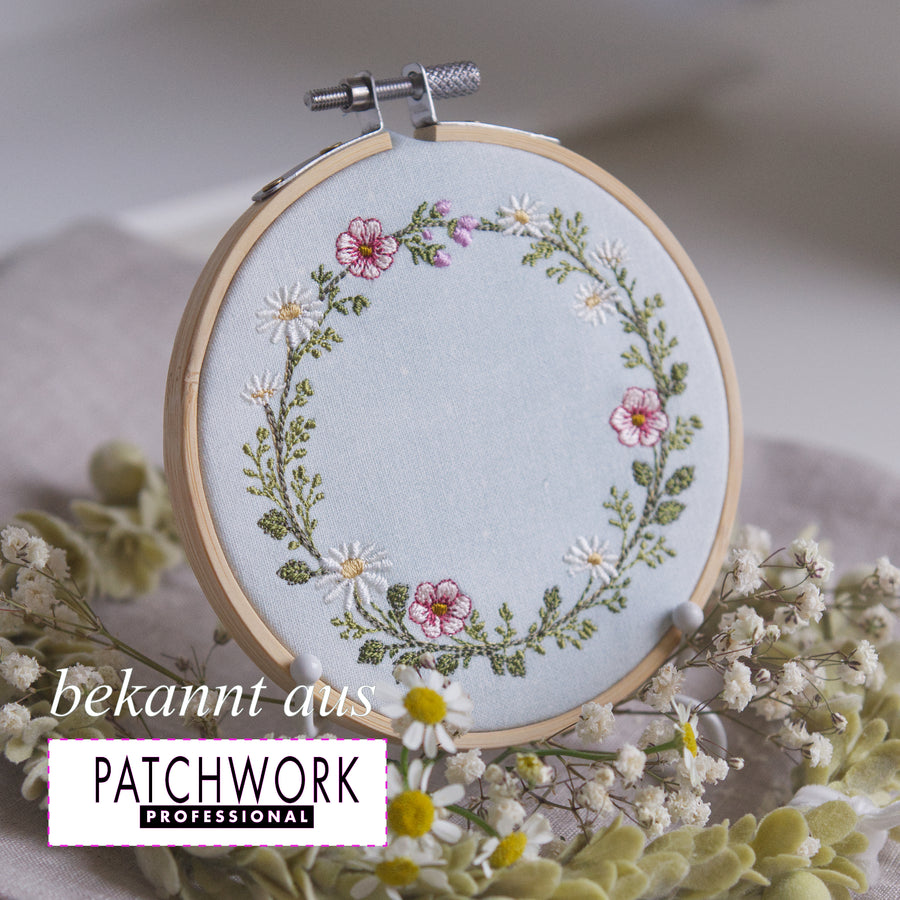 Stickdatei Wiesenkranz 10x10 mit Margeriten, rosa Wildblumen und Kräutern als runder floraler Rahmen auf Leinen, ideal für Kissen, Patchwork und personalisierte Stickprojekte im Landhausstil bekannt aus Patchwork Professional